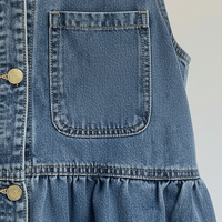 Blue denim mini dress with button front, pockets, and straps, front view on model.