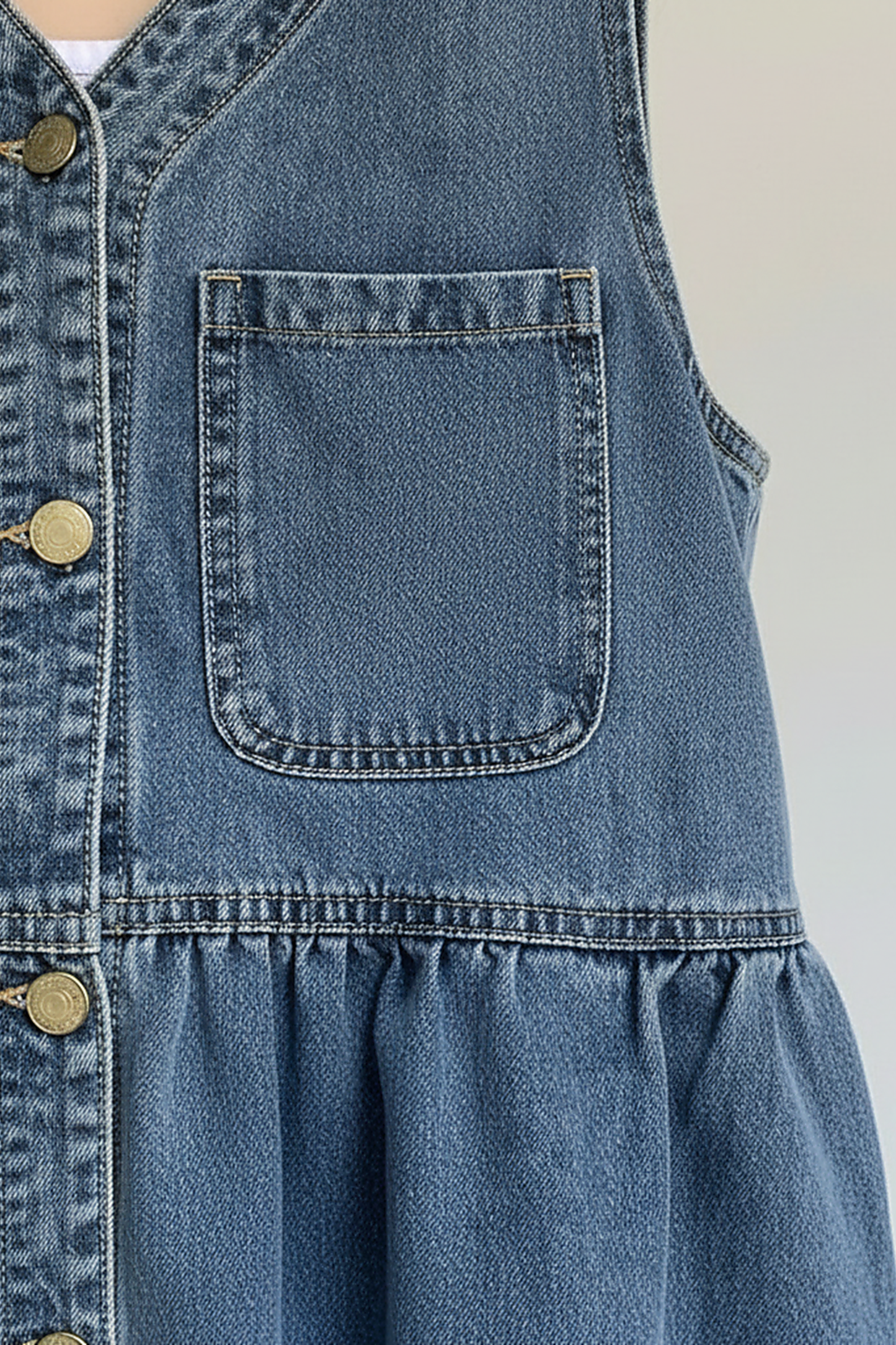 Blue denim mini dress with button front, pockets, and straps, front view on model.