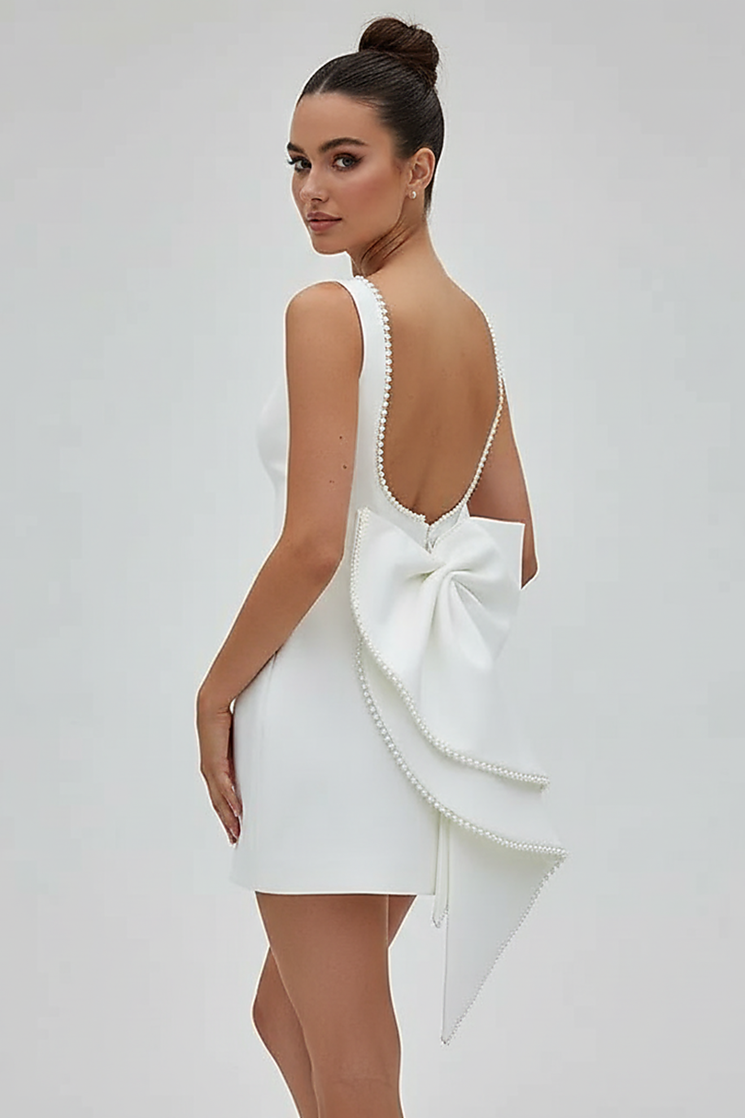 White mini dress with bow and pearl detail, front view on model.